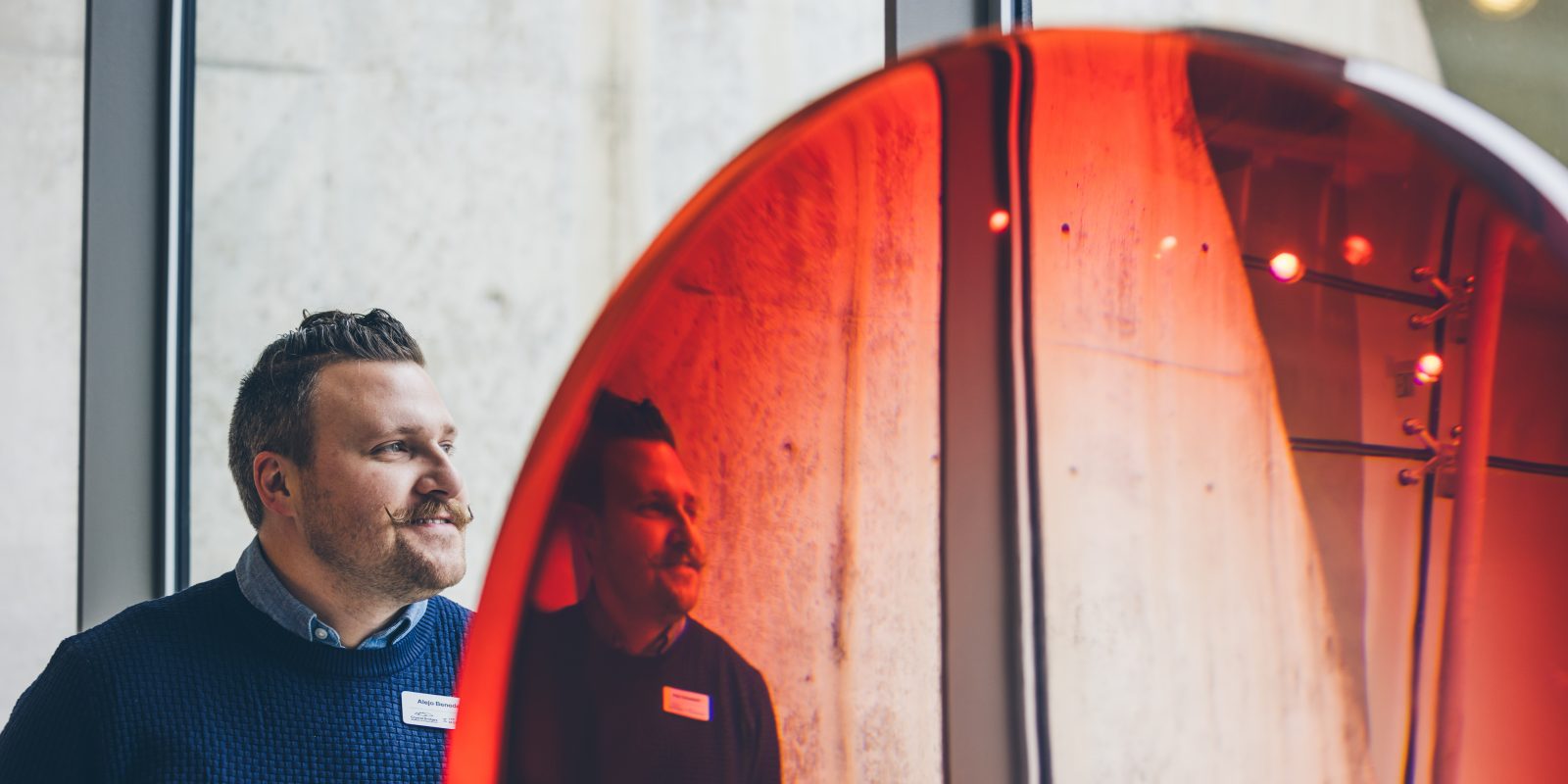 Distorted photo of TCU alum and art curator Alejo Benedetti standing next to a red, semi-transparent glass-like object.