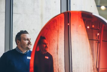 Distorted photo of TCU alum and art curator Alejo Benedetti standing next to a red, semi-transparent glass-like object.