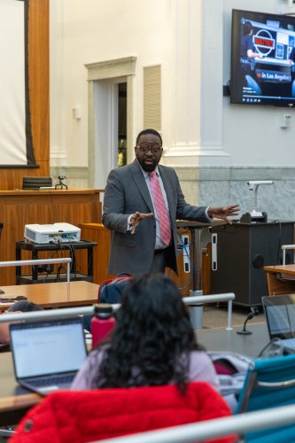 Photograph of Judge Zuberi Williams wearing a suit and tie while teaching a college class.