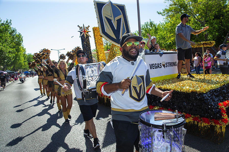 Photograph of people dressed in Vegas Golden Knights attire and holding team signs while participating in a parade.