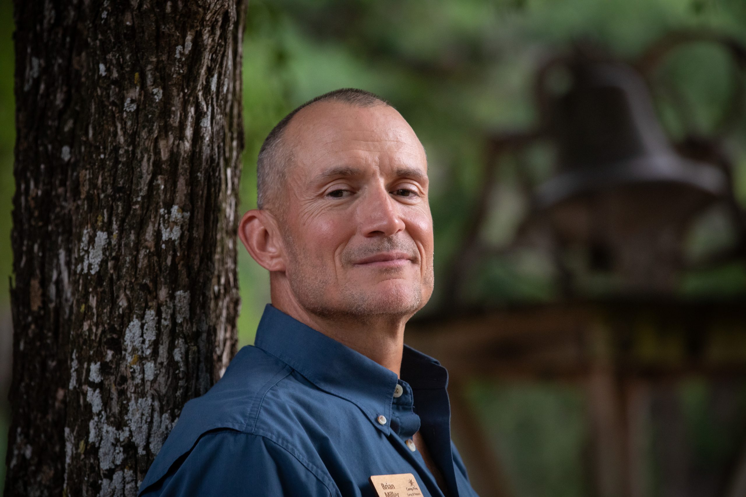Close-up portrait of TCU alum Brian Miller standing against a tree trunk, chin raised and wearing a slight smile.