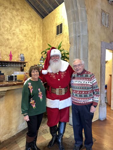 Photograph of two TCU alumnae wearing Christmas-themed sweaters, standing next to a person dressed as Santa Claus.