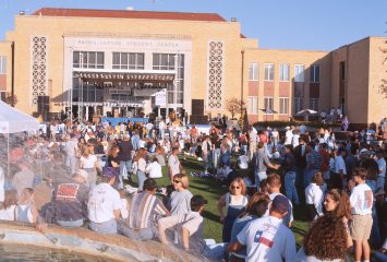 Outdoor photo of Frog Fountain on TCU’s campus in the 1990s, with the Brown-Lupton Student Center in the background and dozens of students gathered in the foreground.