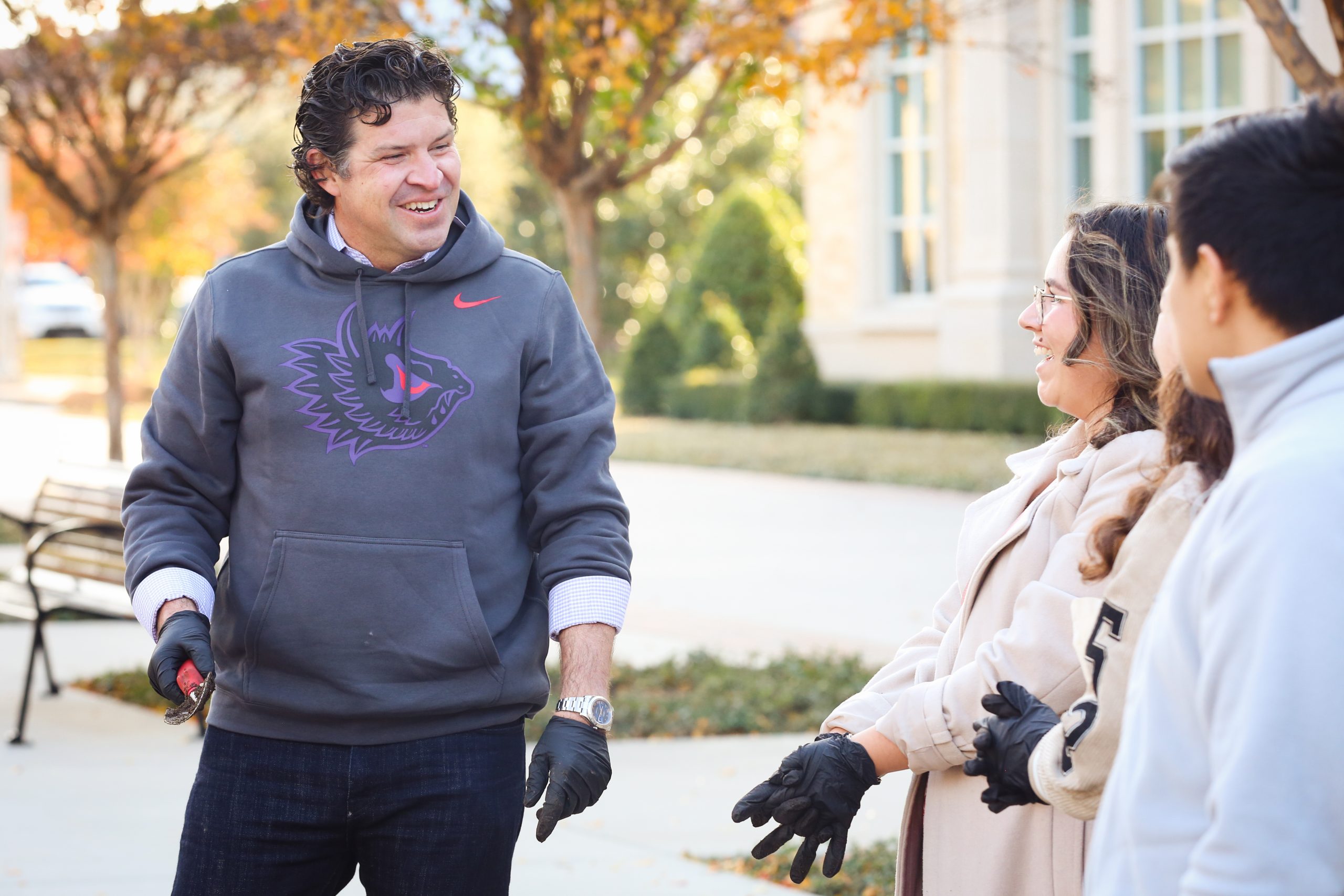 Photograph of TCU Chancellor Daniel Pullin, wearing a TCU Athletics sweatshirt, planting tulips alongside other community members on a sunny day.
