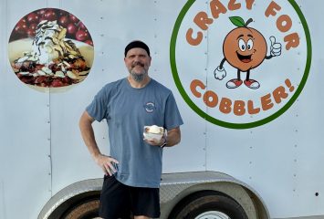 TCU alum Adrian Gonzalez holds a bowl of cobbler in front of a trailer with a cartoon peach logo and the text "Crazy for Cobbler!"