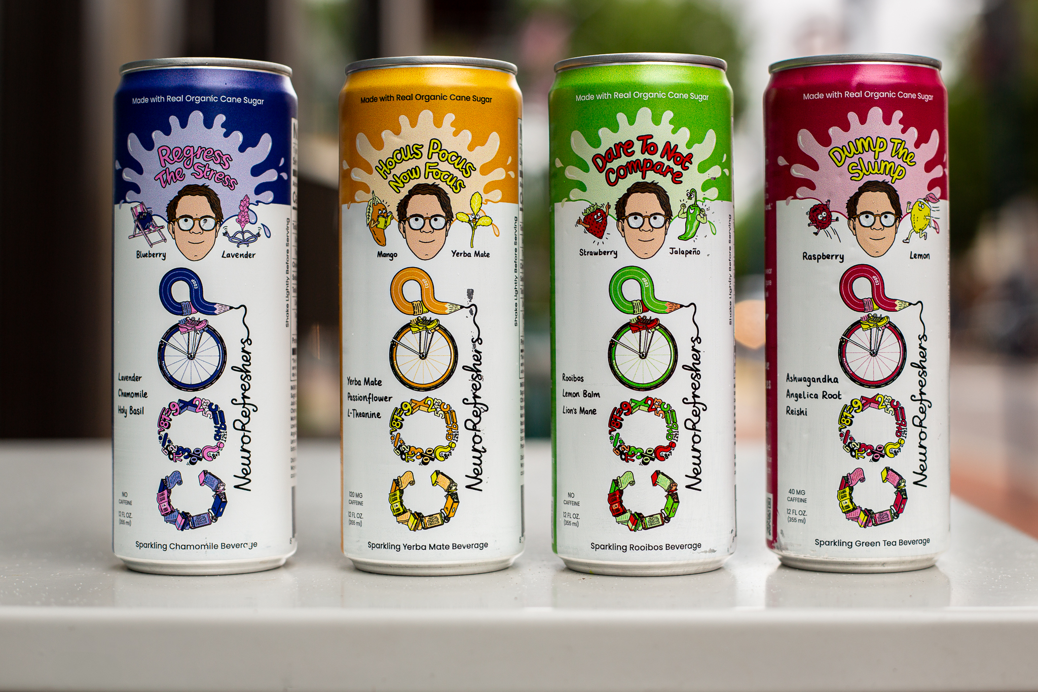 Photograph of four colorful cans of Coop NeuroRefreshers beverages arranged outdoors against a blurred street backdrop.