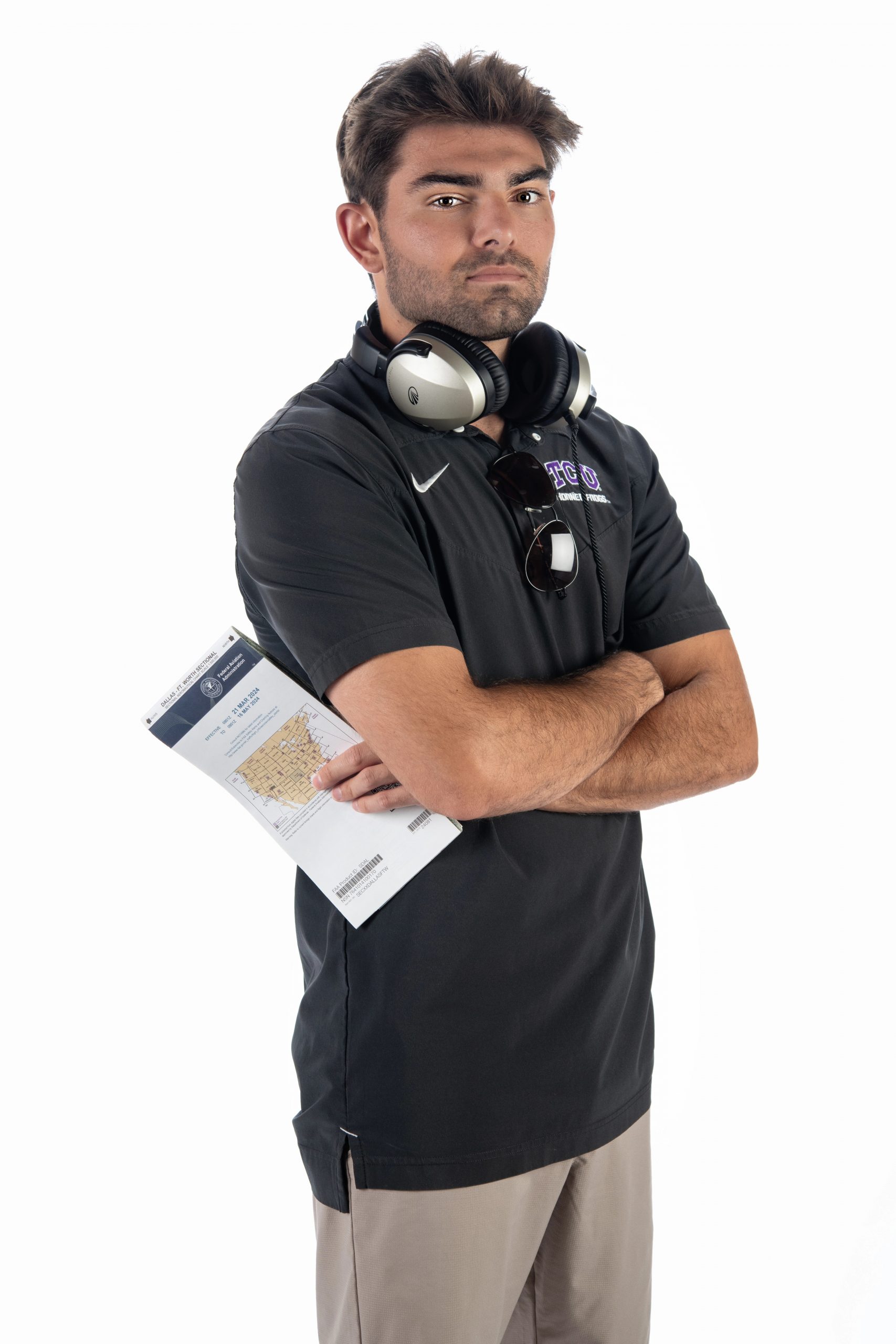 Photograph of TCU student Matthew Miamidian standing against a white backdrop, holding an aviation map with his arms crossed over his chest.