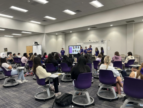 Photograph of TCU Pre-Health Ambassadors speaking with Paschal High School students seated in a large carpeted room about pursuing a pre-health track in college.