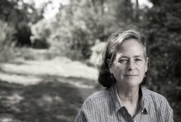 Black-and-white photograph of author Catherine O’Connor looking toward the camera, with a shadowy wood backdrop behind her.