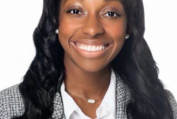 Photograph of TCU alumna Angel Guyton smiling toward the camera against a white background, wearing a white collared shirt and a black-and-white checkered blazer.