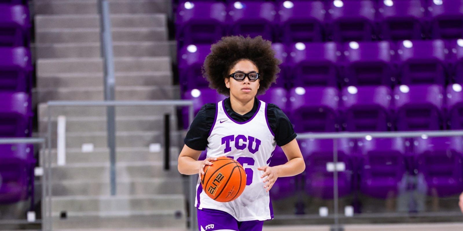 Photograph of Olivia Miles in a white TCU practice jersey dribbling down the court, a large purple TCU logo at center. Purple arena seats fill the background.