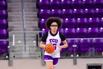 Photograph of Olivia Miles in a white TCU practice jersey dribbling down the court, a large purple TCU logo at center. Purple arena seats fill the background.