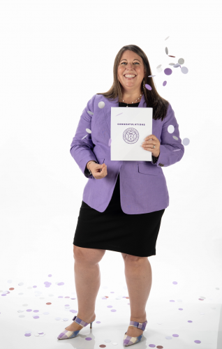 Studio portrait of TCU Dean of Admission Mandy Castro, wearing a purple sports jacket and black dress, holding an acceptance letter with a purple “Congratulations” heading and seal.