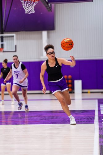 TCU basketball player Olivia Miles corrals a loose ball and turns upcourt during a summer 2025 practice. Two teammates, including Marta Suárez, appear in the background.