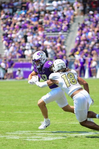 Photograph of then TCU wide receiver Jack Bech in a purple jersey, white helmet and white pants running downfield as a Colorado Buffaloes defender in a white jersey with gold No. 18 pursues him.