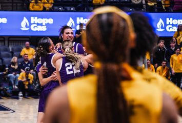 Photograph of TCU women’s basketball players celebrating with Marta Suárez after her game-winning shot against West Virginia in a January 2026 NCAA game. Two West Virginia players in yellow uniforms stand with their backs to the camera in the foreground.