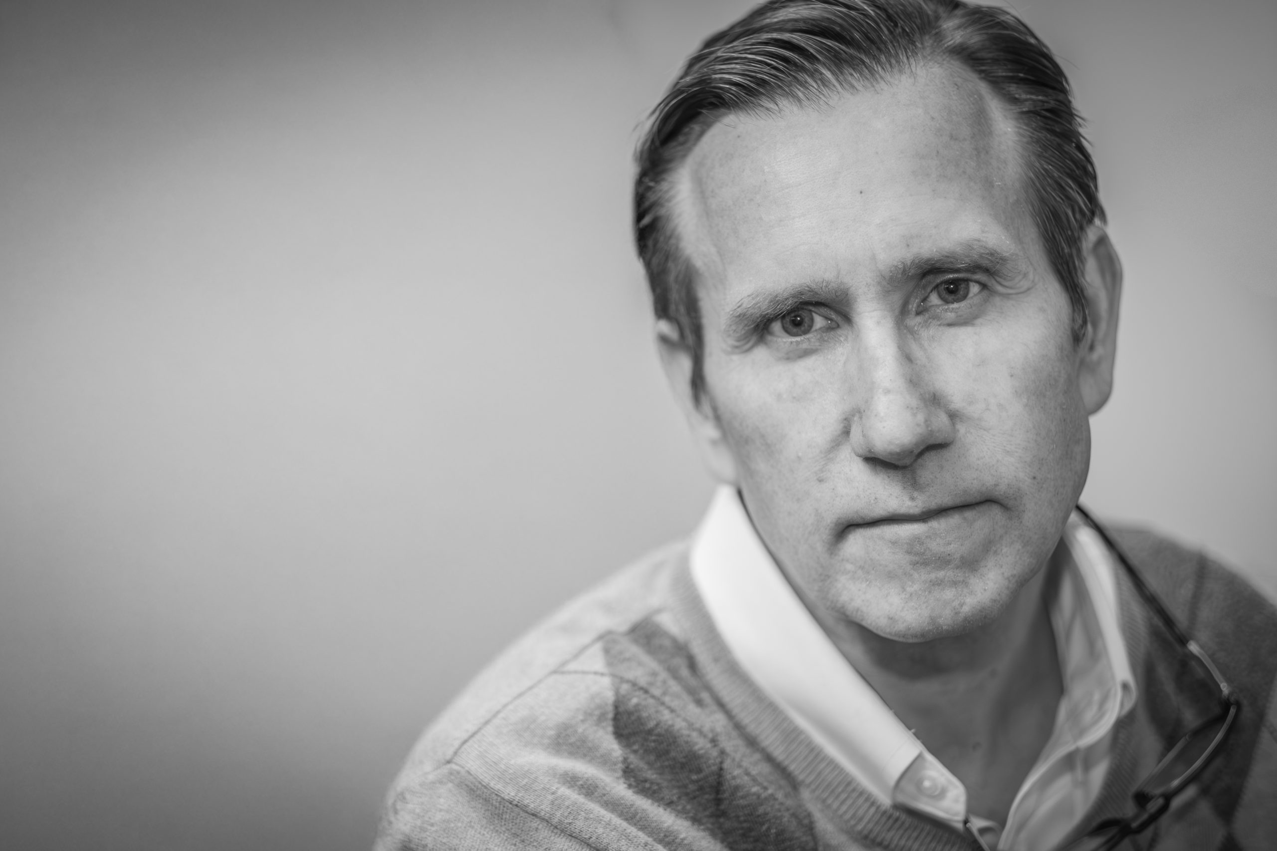 Black-and-white photograph of Christopher Watts, former professor and dean of the Harris College of Nursing & Health Sciences, wearing a white collared shirt and sweater.