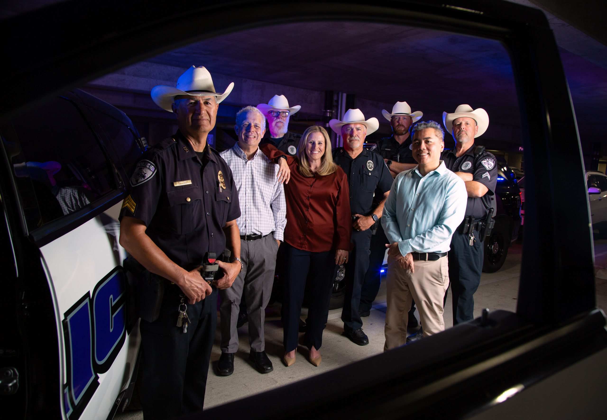 TCU criminal justice professors Johnny Nhan, Ronald Burns and Kendra Bowen stand with North Texas law enforcement officers near a police vehicle in a training facility.