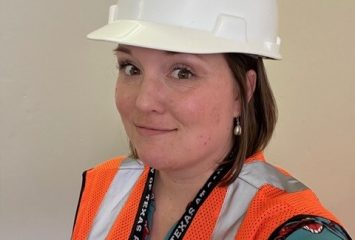 Stephanie Loken Edgett wears a white UTSA hard hat and orange safety vest on a construction site.