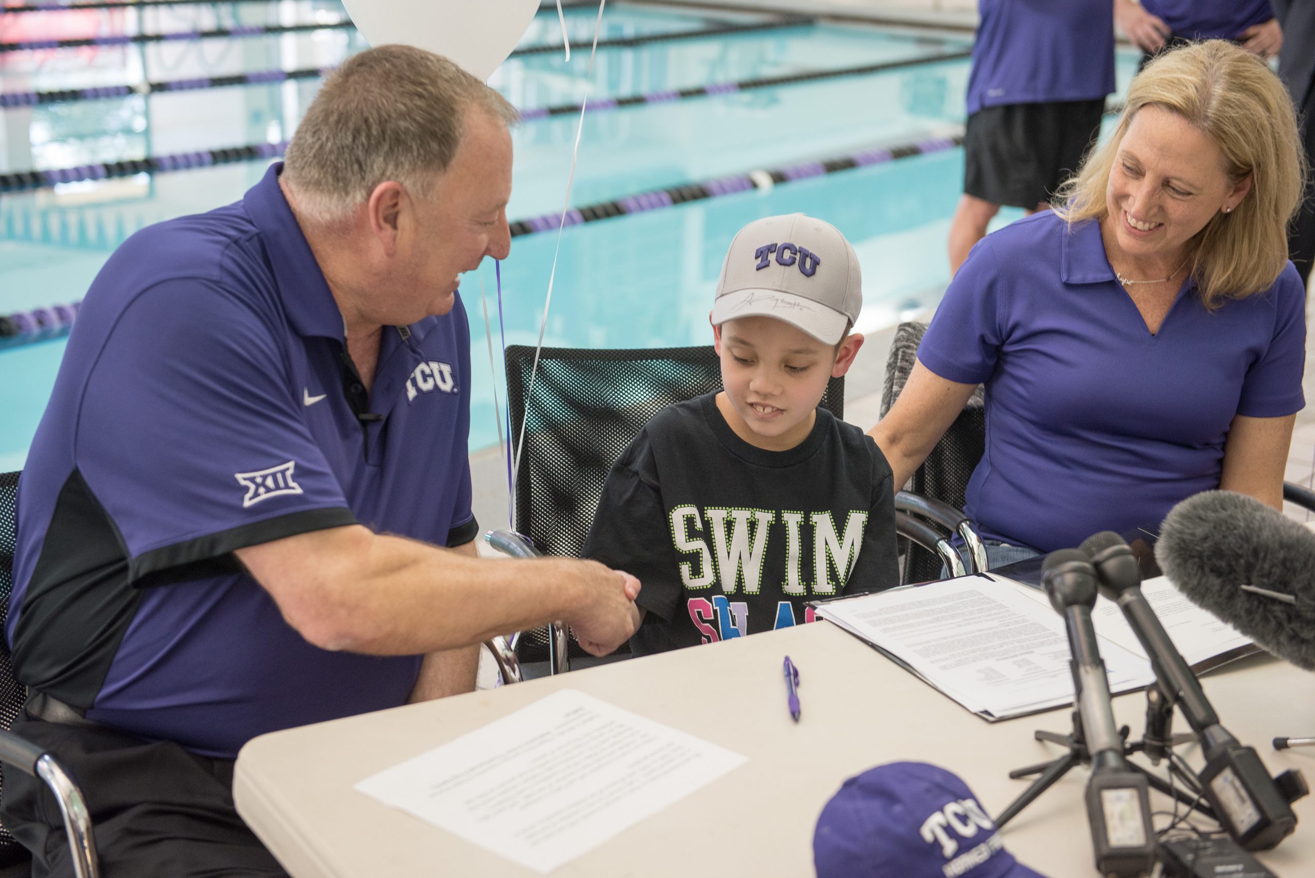 Coach Richard Sybesma and Cathy Boyd Lin ’89 watch as 8-year-old Nathan Lin signs his honorary Letter of Intent to join the TCU swim team at the university pool.
