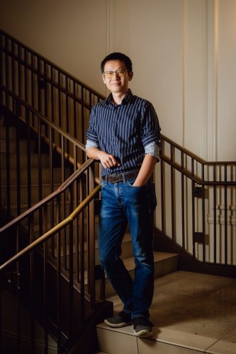 Xiaolu Zhou stands on a staircase in a TCU building, leaning against the railing.