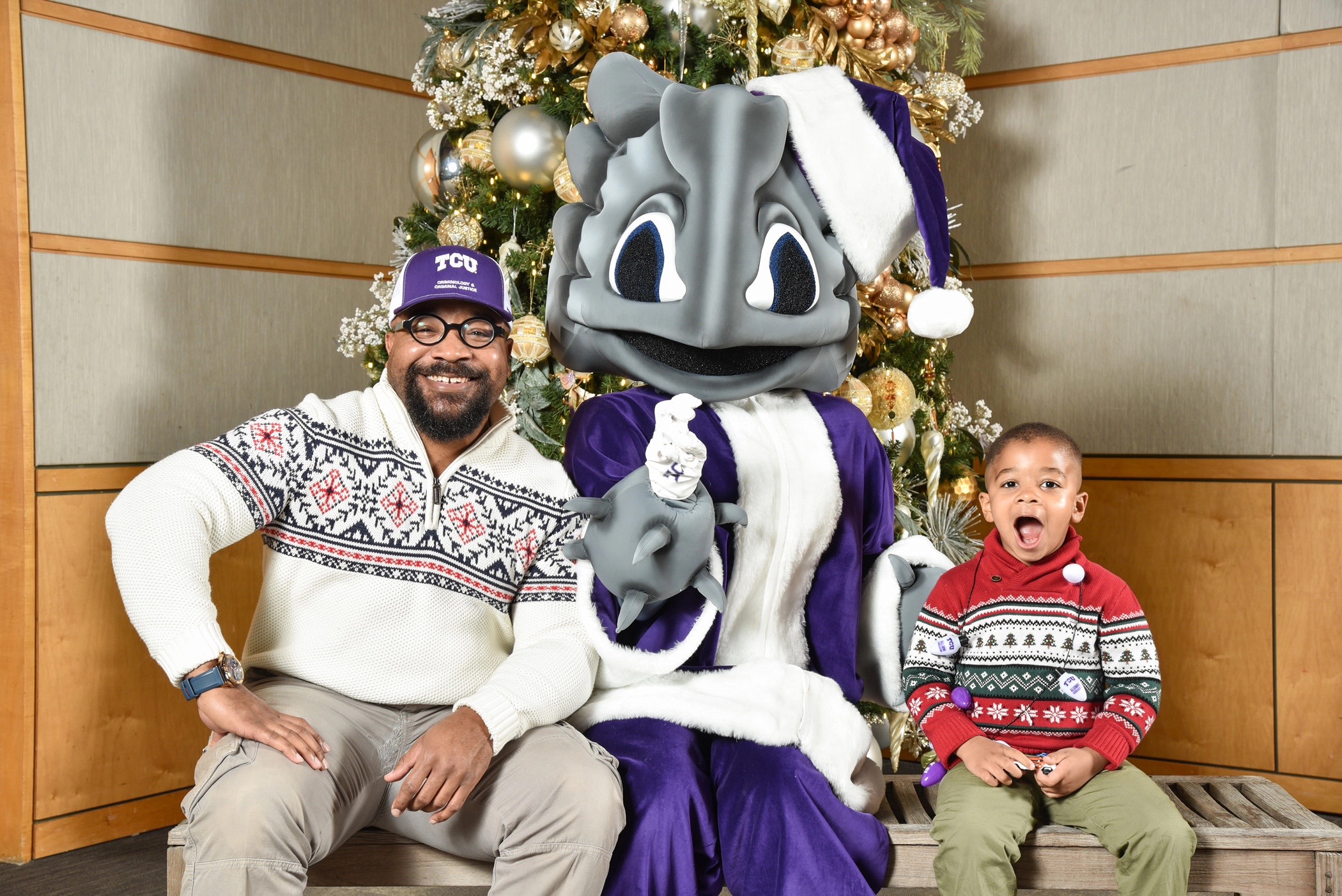 Man and child pose with Super Frog mascot dressed as Santa in front of a decorated Christmas tree.