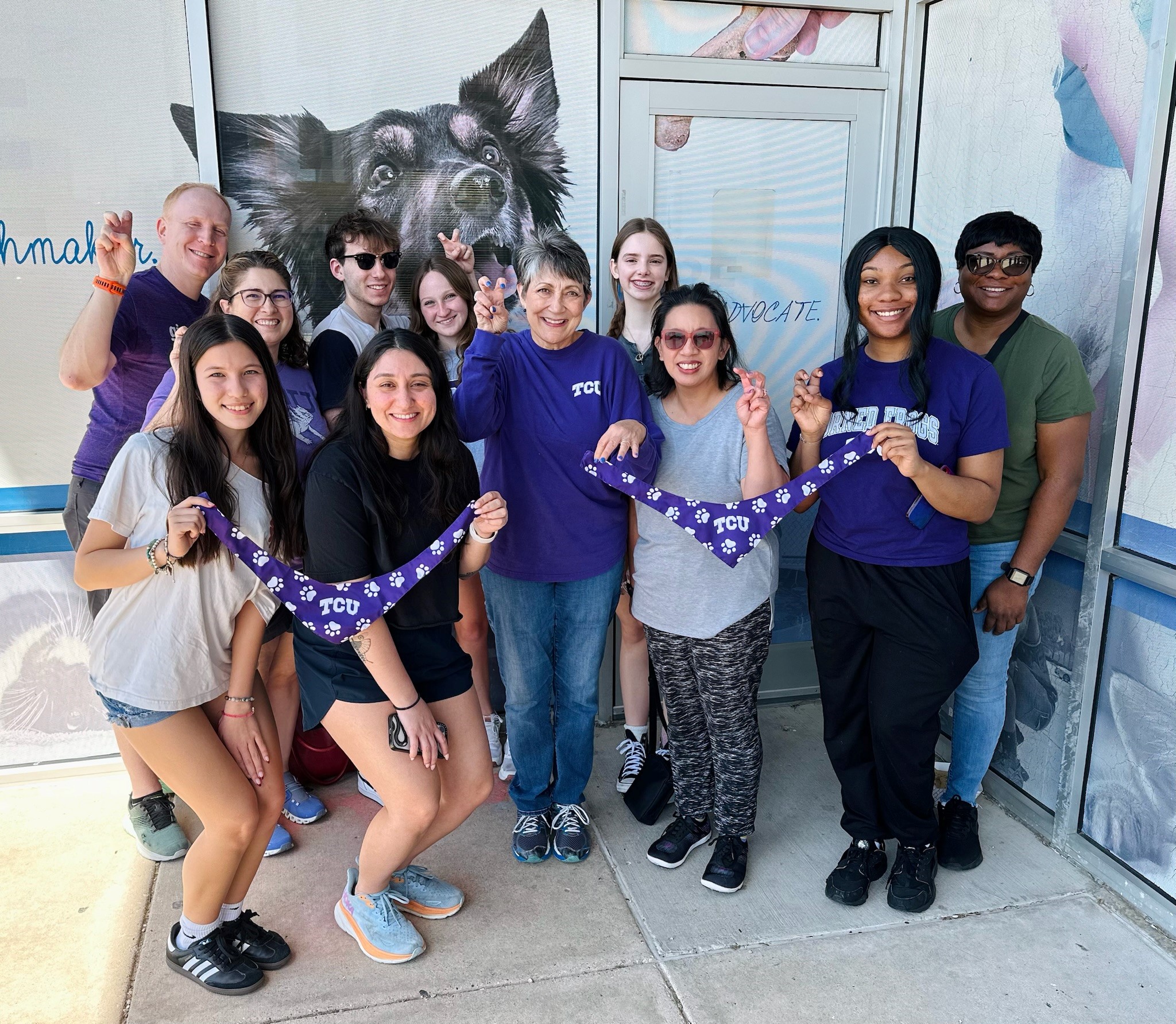 Group of TCU alumni volunteers holding purple TCU paw print bandanas outside Dallas Animal Services