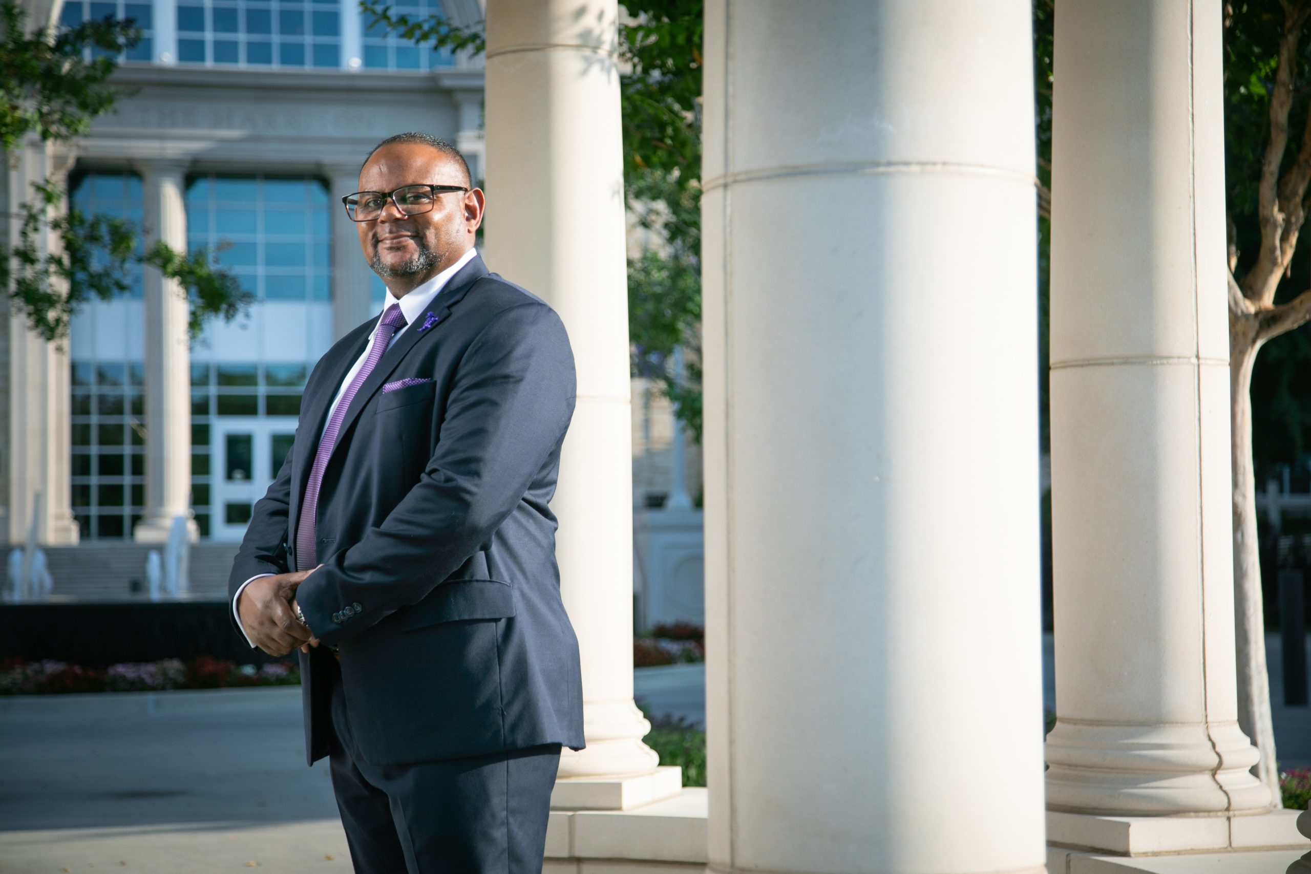 Floyd L. Wormley Jr., TCU's provost and vice chancellor for academic affairs, stands in a suit and purple tie between columns of a campus rotunda, with The Harrison building visible in the background on TCU's campus in Fort Worth, Texas.