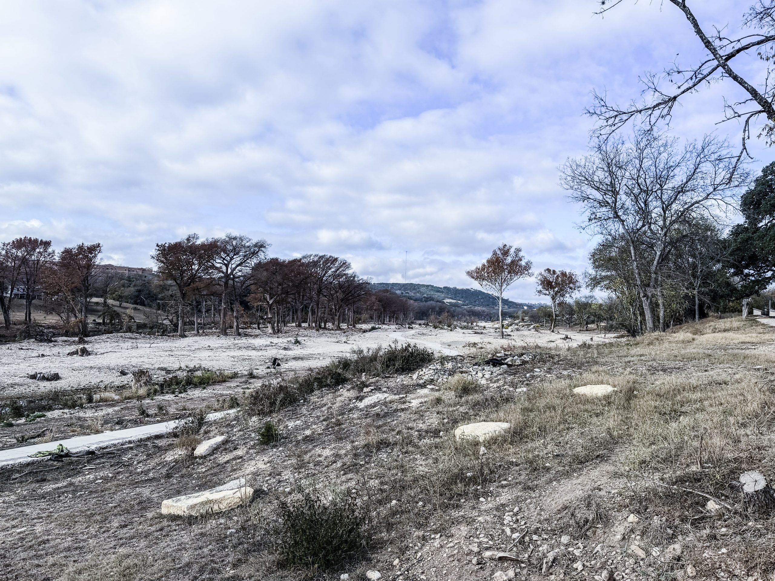 A wide view of the flood-ravaged landscape at Louise Hays Park in Kerrville, Texas, showing barren ground, tree stumps, scattered rocks and debris stretching across the once-lush 64-acre park months after the July 4 Guadalupe River flood.
