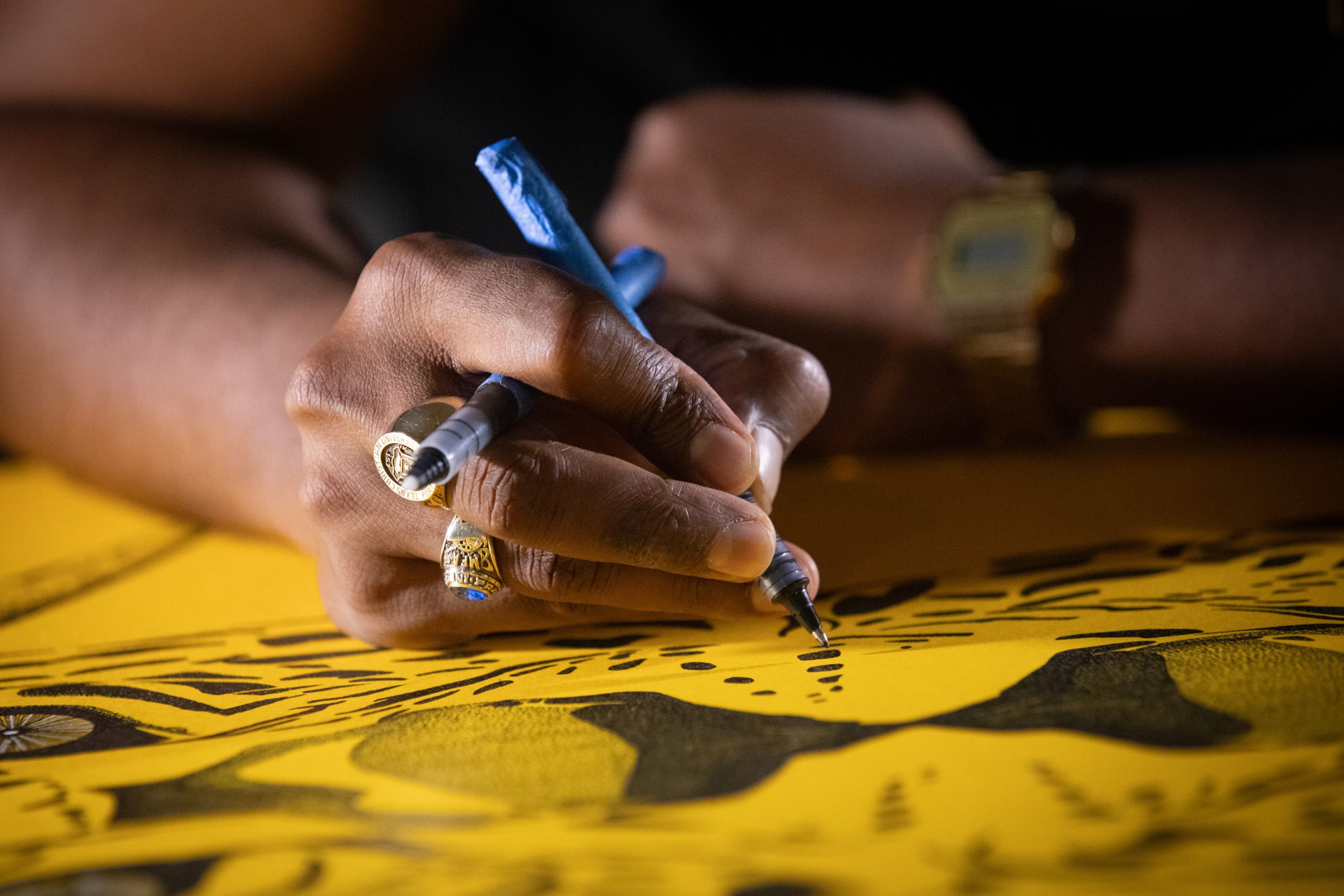 Artist DJ Perera uses a pen to create intricate stippled dot work on yellow paper.