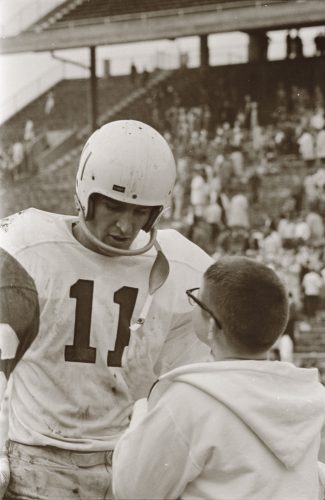 TCU quarterback Sonny Gibbs, wearing No. 11, shares a moment with a young boy on the sideline as a packed stadium crowd looks on, early 1960s.