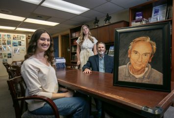 Boller Review editor Trinity Sloan, former editor Lexie Woodall ’25, and Dr. Dan Williams, director of TCU Press, pose with a portrait of Paul F. Boller Jr., the namesake of the TCU publication dedicated to undergraduate research, in the offices of TCU Press,