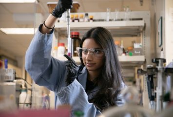 Student researcher Saba Anjum uses a pipette while conducting laboratory research, wearing safety goggles, gloves and a lab coat.