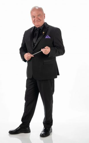Bobby Francis, wearing a black suit with purple pocket square, holds a conductor's baton in a studio portrait.