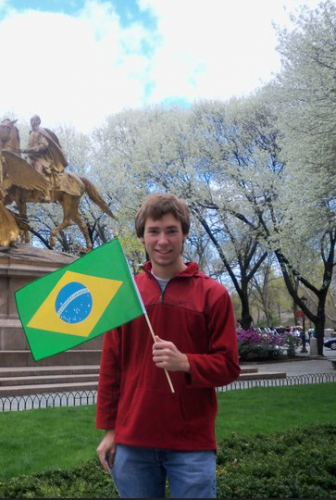 A young Pearce Edwards holds a Brazilian flag while standing in front of a statue in a park.