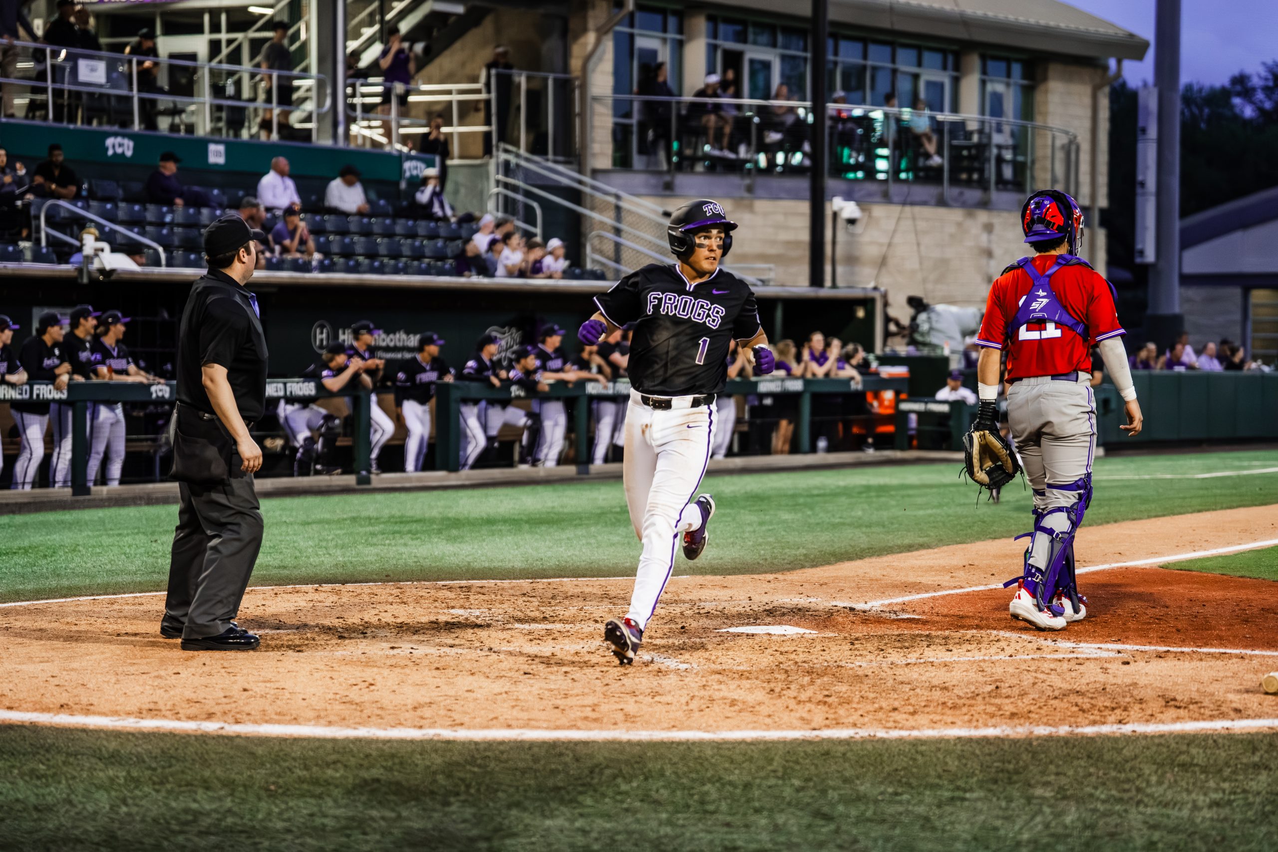 TCU baseball player Jack Bell scores a run at home plate at Lupton Stadium, with an umpire and opposing catcher looking on.