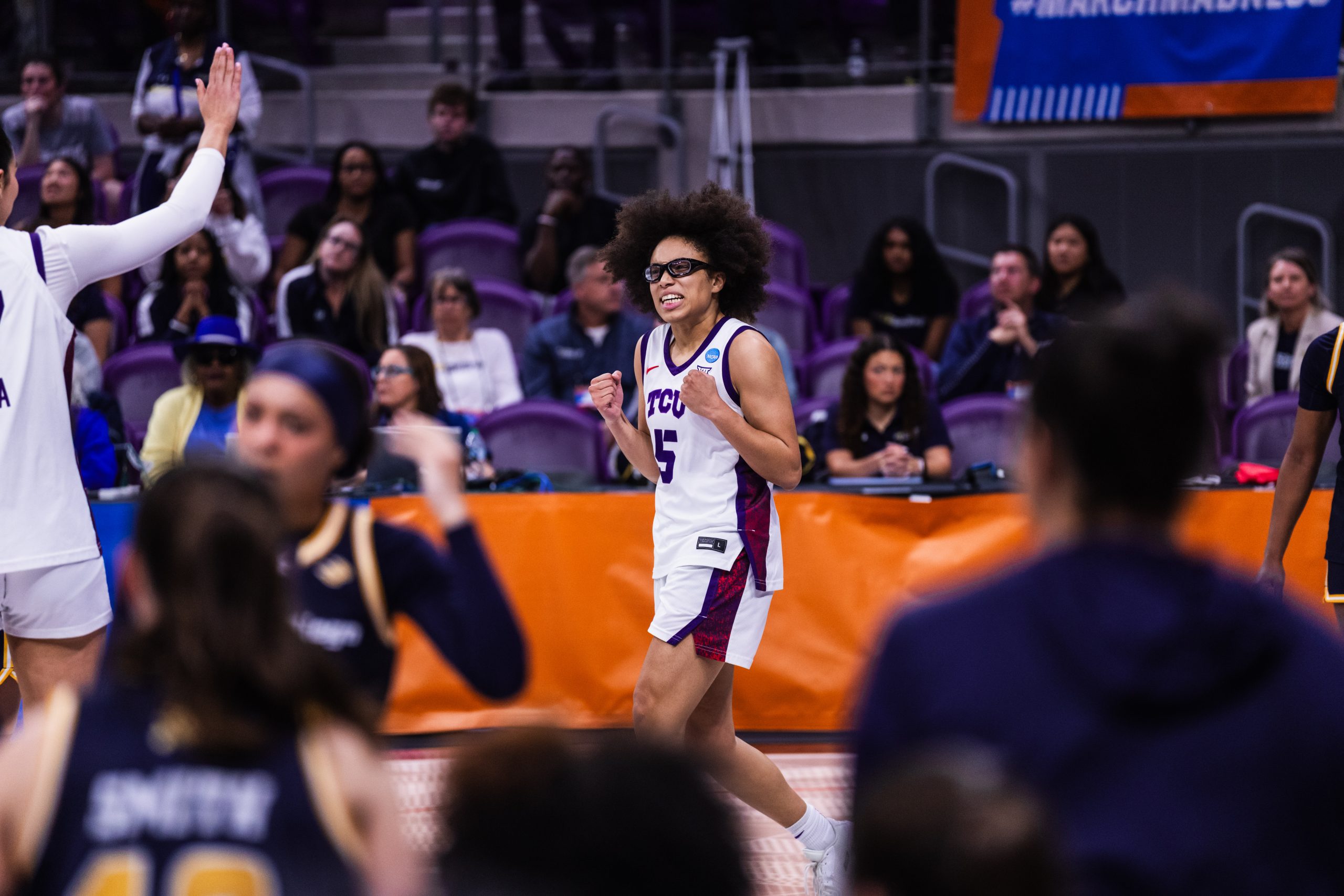 TCU women’s basketball player Olivia Miles pumps her fists in celebration during the NCAA Tournament, with a teammate raising a hand for a high-five in the foreground.