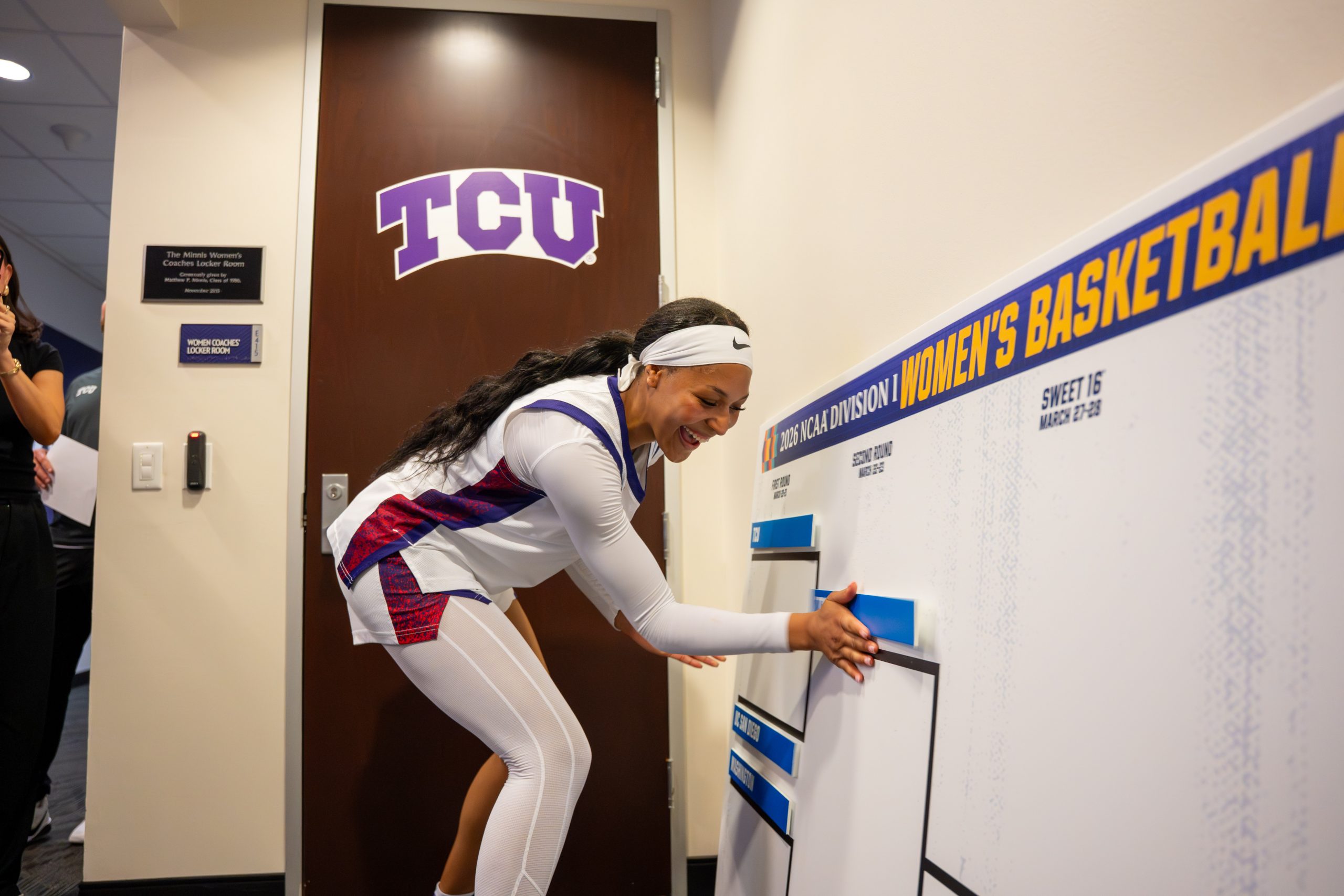 TCU women’s basketball player Taylor Bigby smiles while placing her team’s name on the 2026 NCAA Division I Women’s Basketball Tournament bracket, advancing TCU to the second round.