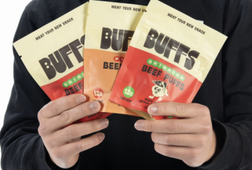 A person holds three bags of Buffs beef puffs fanned out, with the “Meat Your New Snack” tagline visible across the tops.
