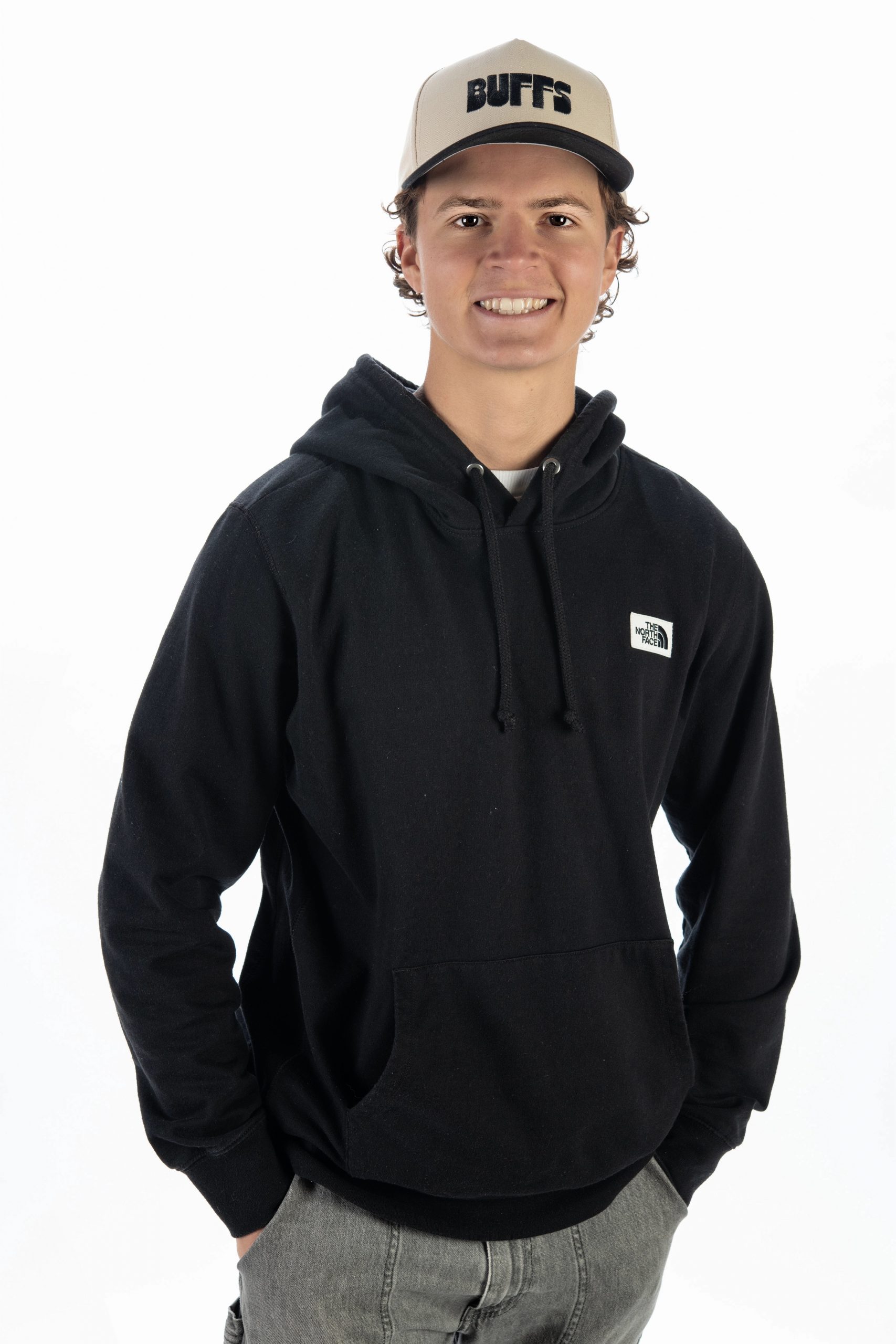 TCU senior Beckett Kitaen smiles in a studio portrait, wearing a black hoodie and a tan cap with the Buffs logo.