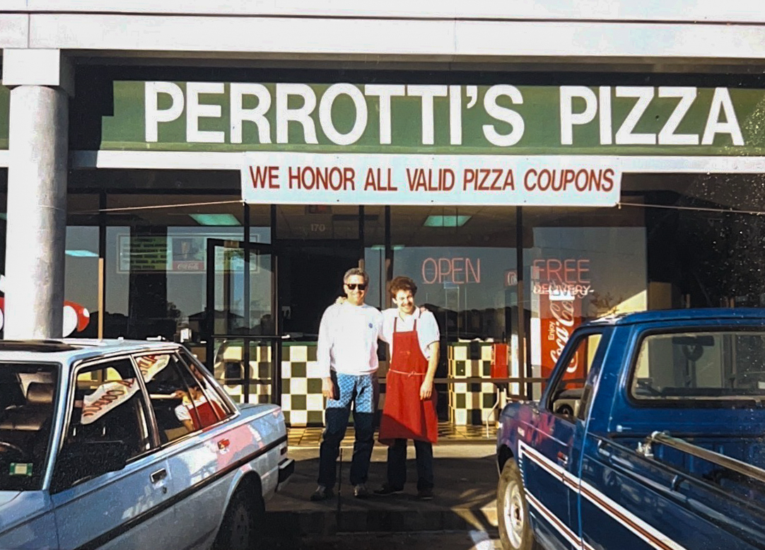 Richard Perrotti Sr., left, and Richard Perrotti Jr., right, stand outside a former Perrotti’s Pizza location in Fort Worth on a sunny day in the 1980s. A green “Perrotti’s Pizza” sign hangs above them.