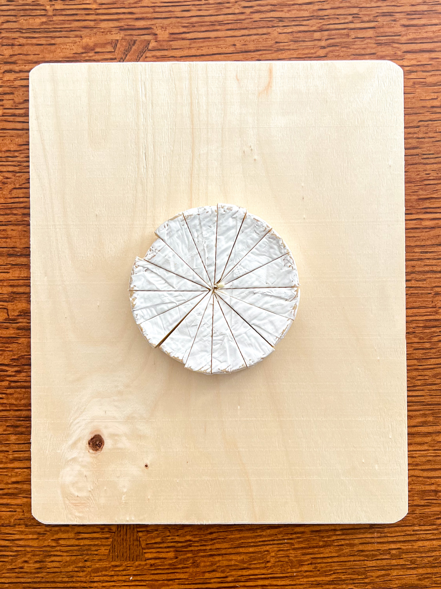 A wheel of brie cut into small triangular wedges, placed on a light wood serving board.