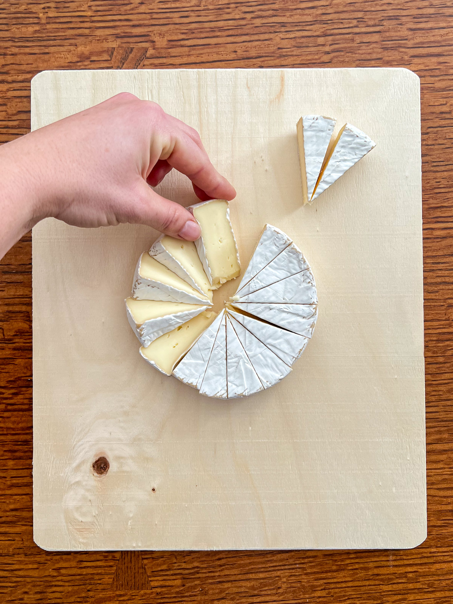 A hand twists wedges of brie on their sides to create a pinwheel arrangement.
