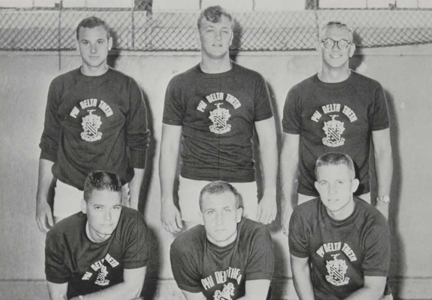 Black-and-white yearbook photo of six young men posed in two rows in front of a chain-link fence, all wearing Phi Delta Theta t-shirts with the fraternity’s crest.