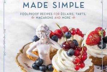 Cover of “French Pastry Made Simple: Foolproof Recipes for Éclairs, Tarts, Macarons and More” by Molly Wilkinson, with cream-topped pastries garnished with berries and cherries arranged on a floral cake stand alongside a small porcelain figurine.
