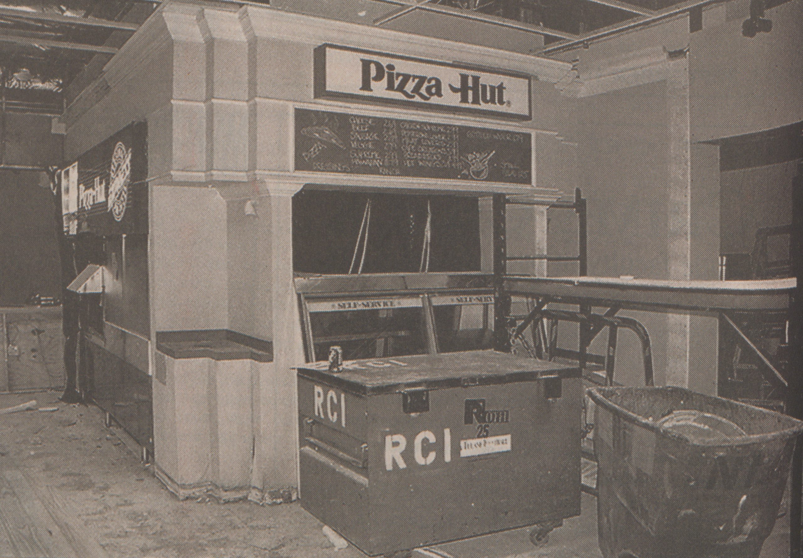 Black-and-white photo of a Pizza Hut counter under construction in the TCU Student Center, with the Pizza Hut sign and menu board mounted above empty shelves, a self-serve display and a construction dumpster marked "RCI" in the foreground. Published in The Skiff, Sept. 10, 1999.