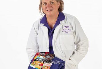 Lori Borchers, TCU nursing scholar, holds folded purple scrubs topped with packaged snacks including trail mix, beef jerky and tuna.
