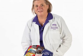 Lori Borchers, TCU nursing scholar, holds folded purple scrubs topped with packaged snacks including trail mix, beef jerky and tuna.