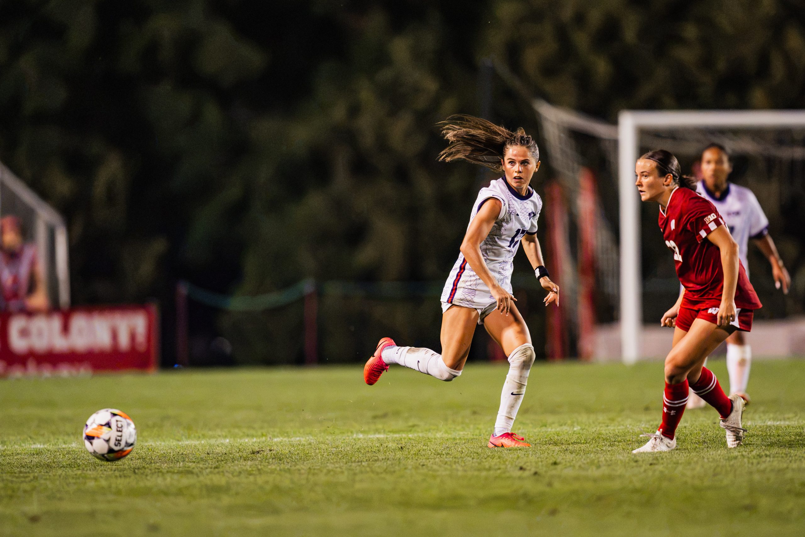 Cameron Patton chases a loose ball during a night match, with an opposing player in a red uniform nearby.
