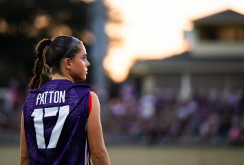 Cameron Patton looks over her shoulder in a purple TCU jersey at dusk, with spectators blurred in the stands behind her.